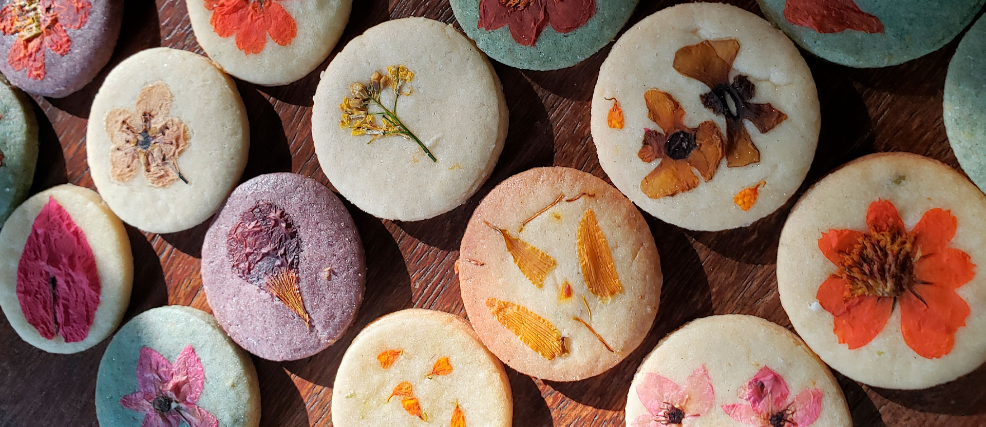 Biscoitos florais em diferentes cores, decorados com flores e pétalas